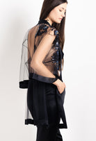 Woman wearing a black sheer jacket with floral embroidery and black silk pants